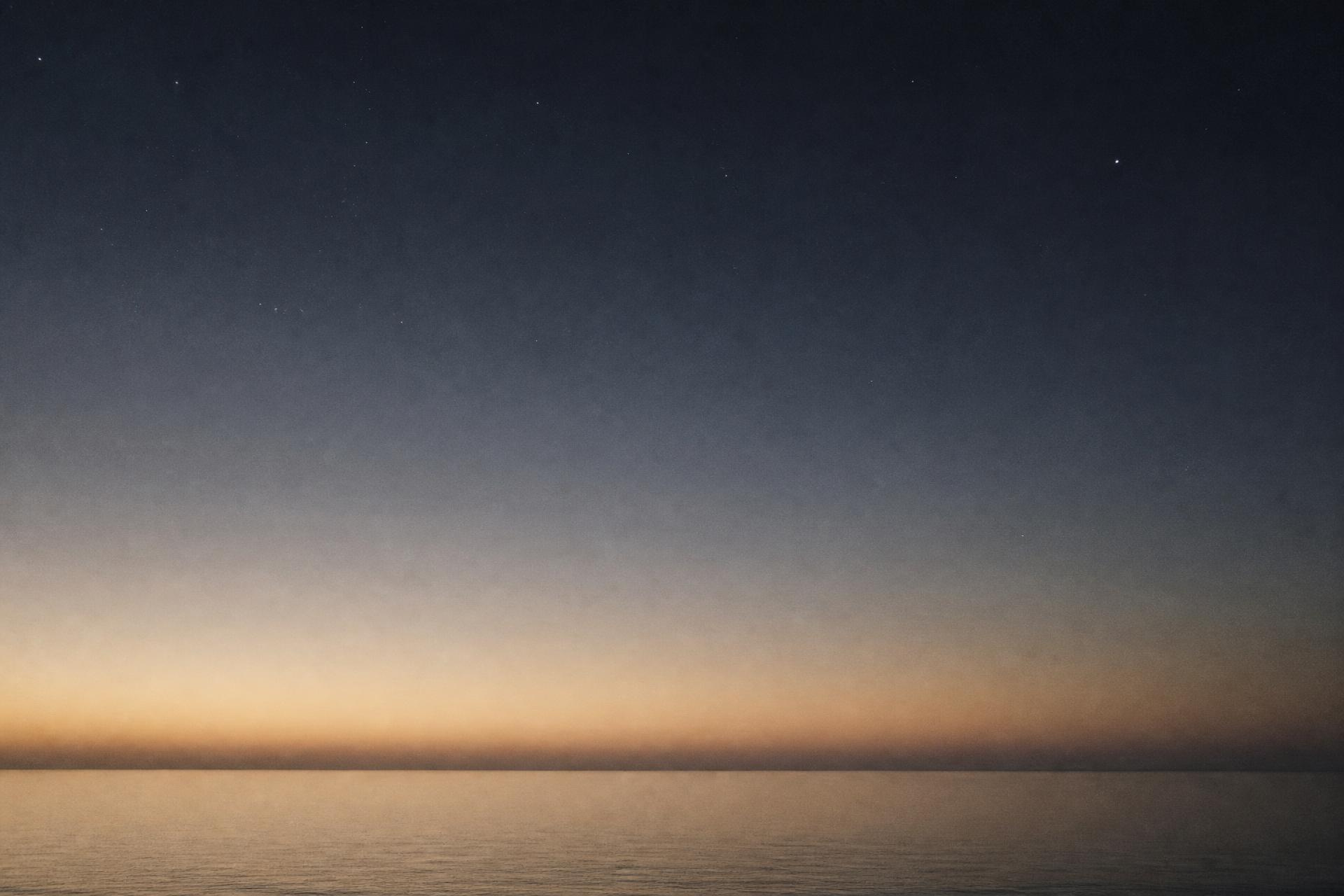 A still ocean horizon beneath a pre-dawn sky scattered with faint stars